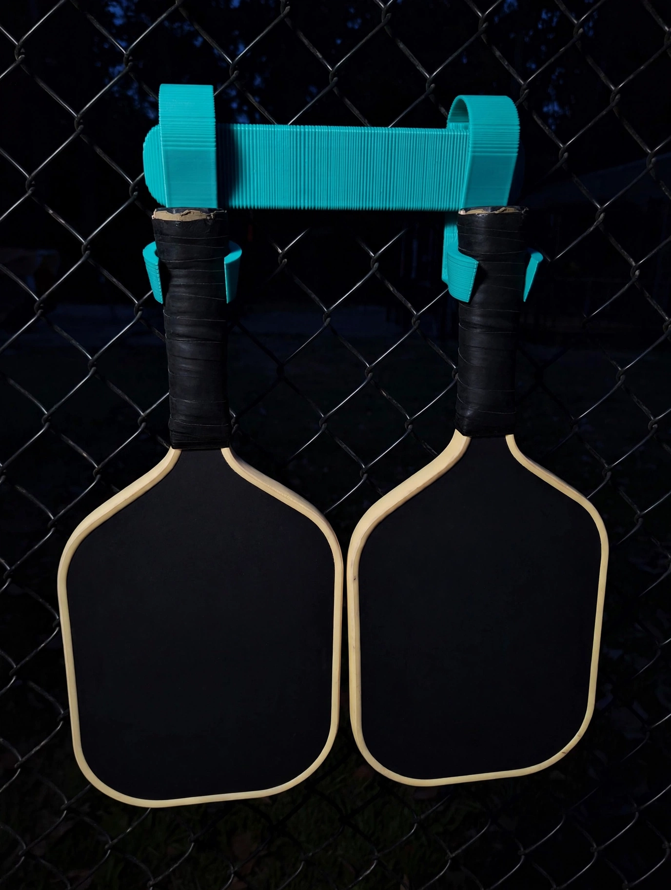 Pickleball Hook Duo holding two paddles on a chain-link fence