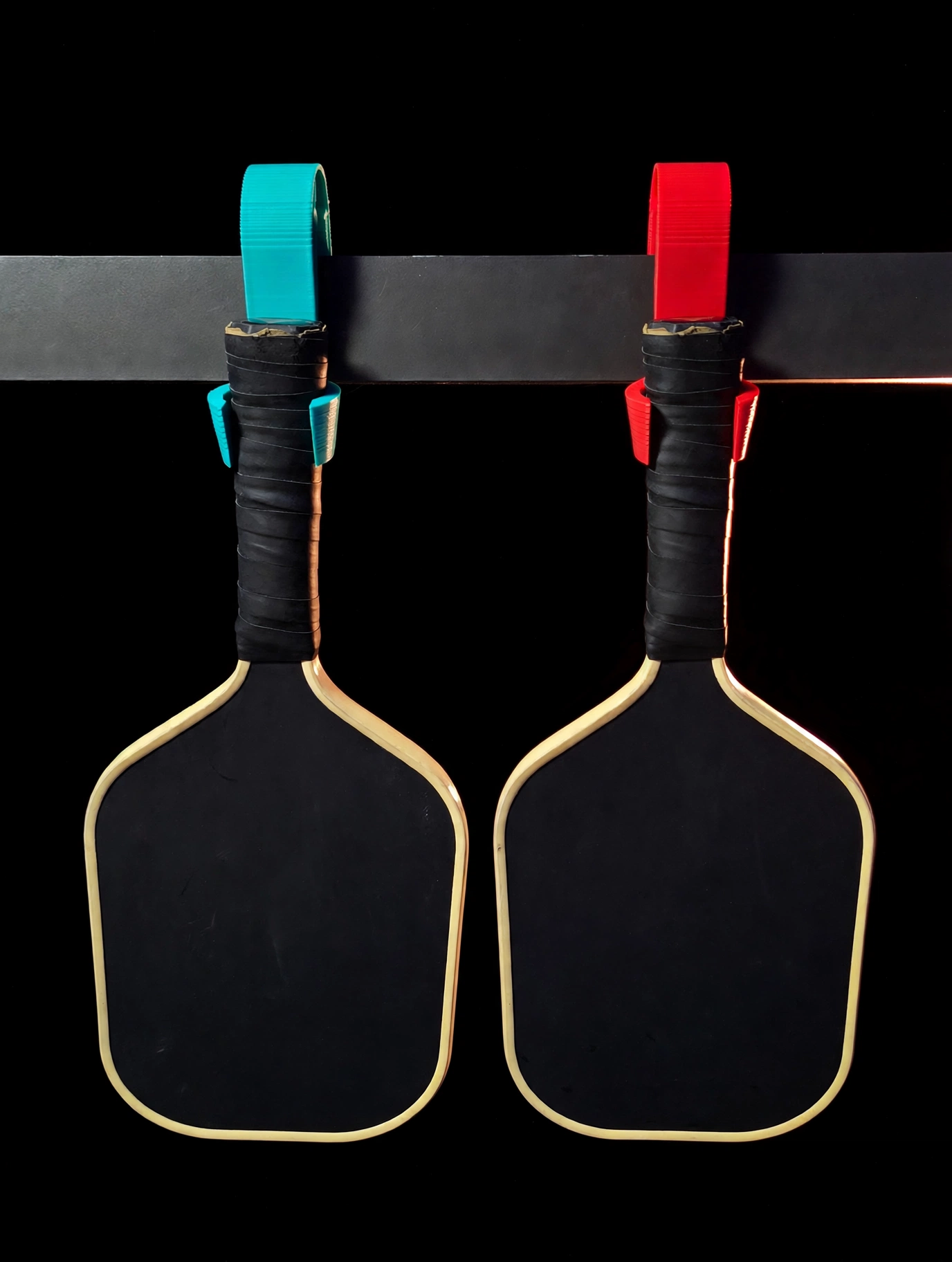 Teal and red Pickleball Hook holders, each holding a paddle